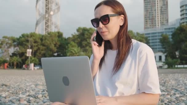 Ευτυχισμένη Καυκάσια Γυναίκα Γυαλιά Ηλίου Που Δουλεύει Φορητό Υπολογιστή Μιλάει — Αρχείο Βίντεο