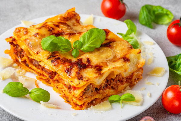 Close up of meat lasagna with fresh basil, tomatoes and parmesan cheese in a plate. Italian cuisine. Delicious food for dinner.