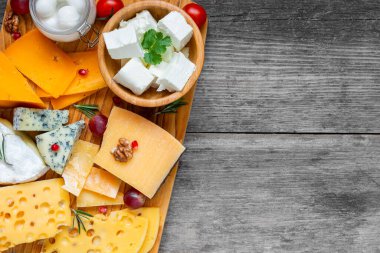 Peynir tahtası. Tahta kesme tahtasındaki peynir çeşitleri. Üzüm meyvesi, domates ve biberiyeyle servis edilen peynir tabağı. Kopyalama alanı olan üst görünüm.