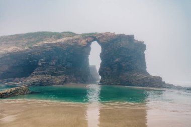 Cathedrals beach in Galicia, Spainn. Foggy landscape with Playa de Las Catedrales Catedrais beach in Ribadeo, Lugo on Cantabrian coast. Natural archs of Cathedrals beach. Moody rock formations on clipart