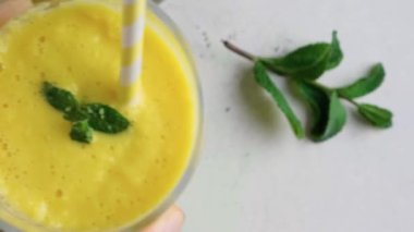 En tepedeki adam masaya bir bardak sarı mango kokteyli ya da naneli ve samanlı milkshake koyar. Tropik sağlıklı içecek konsepti. Yaz içeceği.