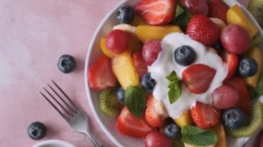 Pembe arka planda yoğurtlu yaz taze meyve salatası. Üst Manzara. Kahvaltı için sağlıklı yemek. Diyet öğle yemeği için karışık çilek, üzüm, muz, kivi, yabanmersini, şeftali, kumkat ve nane..