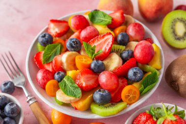 Pembe arka planda çatallı bir kasede yaz meyve salatası. Kahvaltıda sağlıklı vejetaryen yemeği. Vejetaryen diyeti öğle yemeği için karışık tropikal meyve meyvesi. Kapat..