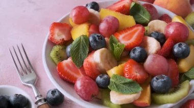 Pembe arka planda bir kasede yaz meyve salatası. Kahvaltı için sağlıklı diyet yemeği. Diyet öğle yemeği için meyve, böğürtlen ve nane.