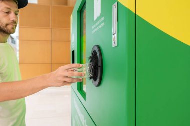 Adam plastik şişeyi ters satış makinesine koyuyor. Erkek atığı azaltmak için tekrar kullanılabilir şişeyi geri dönüşüm makinesine sokuyor. Çevre koruma ve sürdürülebilir yaşam tarzı kavramı.