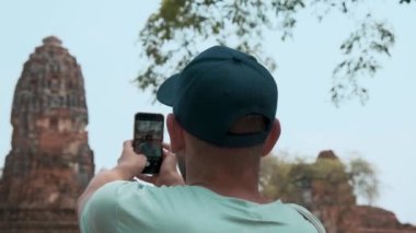 Antik Wat Mahathat tapınağının fotoğrafını çeken turist Ayutthaya tarihi parkında, Tayland 'da. Arkeolojik sitede Budist harabelerini cep telefonuyla fotoğraflayan bir erkek gezgin.