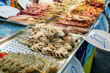 Çeşitli deniz ürünleri ve et şişleri. Çiğ ahtapot, karides ve tahta çubuklarda et. Gece pazarında Tayland yemeği. Phuket, Tayland 'da Asya yemekleri.
