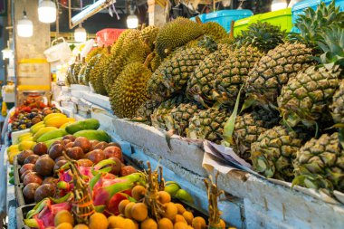 Markette çeşitli taze tropikal meyveler sergileniyor. Taze durian, ananas, mango, longan ve çarkıfelek meyvelerinin renkli görüntüsü Tayland, Phuket pazarında.