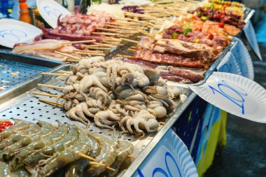 Çeşitli deniz ürünleri ve et şişleri. Çiğ ahtapot, karides ve tahta çubuklarda et. Gece pazarında Tayland yemeği. Phuket, Tayland 'da Asya yemekleri.
