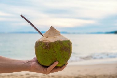 Tayland 'ın Krabi eyaletinde, turkuaz suyla birlikte kumlu tropikal Railay plajında hindistan cevizi suyu tutan bir adam. Yaz içeceği.. 
