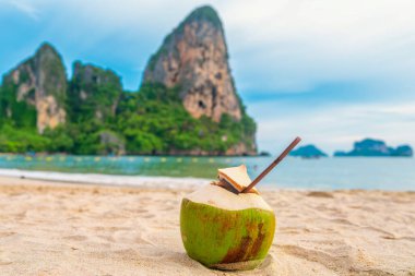 Tayland 'ın Krabi eyaletindeki turkuaz su ve kaya oluşumlarıyla birlikte kumlu tropikal Railay plajında hindistan cevizi suyu içmek. Yaz içeceği.. 
