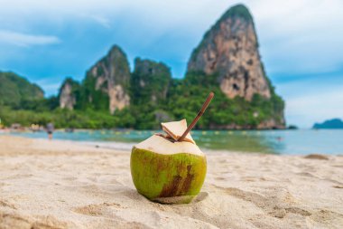 Kumlu tropikal Railay plajında taze hindistan cevizi içeceği, yemyeşil uçurumlar ve arka planda temiz mavi su, Krabi bölgesi, Tayland. Yaz içeceği.. 