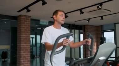 Modern fitness stüdyosunda eliptik makine üzerine kardiyo eğitimi alan bir adam. Erkek, modern spor salonunda eliptik bir antrenörde çalışıyor. Fitness, sağlık, sağlıklı yaşam tarzı konsepti.