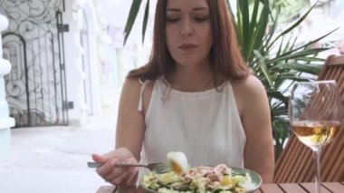 Kafkasyalı kahverengi saçlı kadın öğle yemeğinde dışarıda, kaldırım kafeteryasında otururken sağlıklı nikotin salatası yiyor. Kadın yaz günü restoranda lezzetli diyet yemekleri yiyor.. 