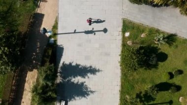 Güneşli bir yaz gününde şehir parkında e-scooter kullanan bir adamın en iyi görüntüsü. İnsansız hava aracı görüntüsü. Erkek, dışarıda elektrikli scooter kullanıyor. Çevre dostu nakliye ve seyahat. Sürdürülebilir yaşam tarzı