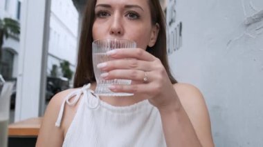 Güzel bir kadın kaldırımdaki kafede otururken ferahlatıcı bir bardak su içiyor. Yaz restoranında susamış bir kadın soğuk bir şeyler içiyor..