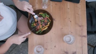 Sağlıklı domuz pastırması salatası yiyen bir kadının öğle yemeğinde dışarıda, kaldırım kafeteryasında otururken gördüğü manzara. Lezzetli yemeklerden hoşlanan bir kadın, restoranda köpüklü beyaz şarap içiyor.