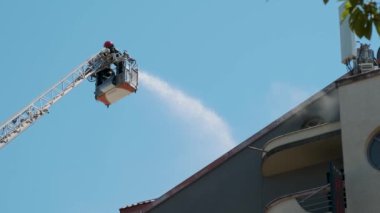 Yüksek platformdaki itfaiyeciler yangın söndürme evlerini su hortumuyla donatılmış geniş merdiven kullanarak binanın çatısına duman püskürterek söndürüyorlar. İtfaiyeci şehirdeki yangını söndürüyor..