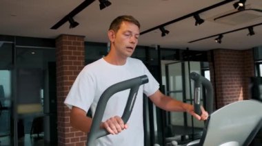 Modern fitness stüdyosunda eliptik makine üzerine kardiyo eğitimi alan bir adam. Erkek, modern spor salonunda eliptik bir antrenörde çalışıyor. Fitness, sağlık, sağlıklı yaşam tarzı konsepti.