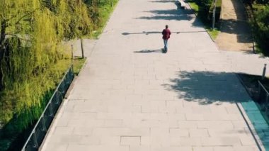 Güneşli bir yaz gününde şehir parkında elektrikli scooter kullanan bir adam. İHA 'dan yüksek açılı görüntü. Erkek, açık havada e-scooter kullanıyor. Çevre dostu nakliye ve seyahat. Sürdürülebilir yaşam tarzı kavramı.