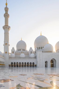 Abu Dabi, BAE 'deki Şeyh Zayed Büyük Camii' nin avlusunda gün batımında beyaz mermer kubbeler, minare ve çiçek mermeri döşemeleri var. İslam sanatı ve mimarisi. Dikey oryantasyon. Popüler Arapça