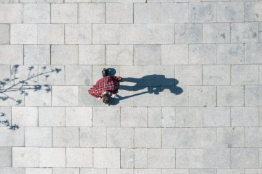 Güneşli yaz gününde, asfaltlı yüzey gölgesinde elektrikli scooter süren bir adamın en iyi görüntüsü. Dışarıdaki e-scooter kullanan erkek manzarası. İHA 'dan sanatsal ve minimal çekim