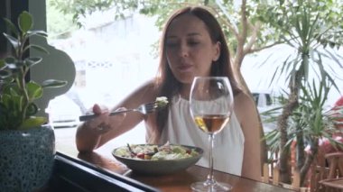 Çekici esmer kadın dışarıda restoranda otururken bir bardak beyaz şarapla sağlıklı nicoise salatası yiyor. Bir kadın yaz günü kafede lezzetli öğle yemeği yiyor.. 