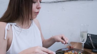 Kafkasyalı kahverengi saçlı kadın öğle yemeğinde şampanya bardağıyla sağlıklı pastırma salatası yerken kaldırımdaki kafede oturuyor. Lezzetli yemeklerden hoşlanan bir kadın, restoranda köpüklü beyaz şarap içiyor.