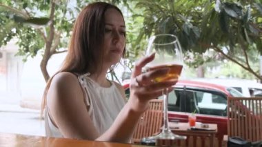 Esmer, beyaz bir kadın öğle yemeğinde beyaz şarap içerken yaz günü dışarıda restoranda oturuyor. Kaldırımdaki kafede içki içen bir kadın, rahatlama anını vurguluyor.