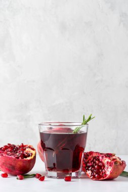 Bir bardak taze nar suyu, nar meyveleri ve gri beton arka planda biberiye. Sağlıklı bir içecek. Dikey yönelim.