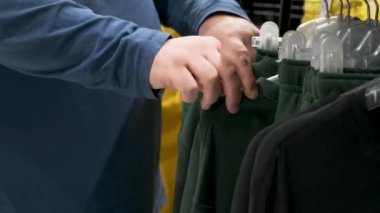Perakende mağazasında elbise seçen bir adam. Erkek el taraması giysiler indirimde, promosyon ve indirim mağazada. Alışveriş ve perakende konsepti.
