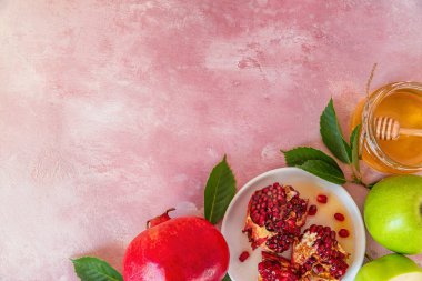 Rosh Hashana Yahudi Yeni Yıl yemeği, bal, nar ve pembe arka planda elmalar. Düz yat. Kopyalama alanı olan üst görünüm.