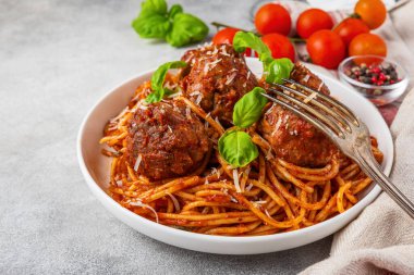 Domates soslu köfteli makarna, üzerinde parmesan peyniri ve çatalla kaplı taze fesleğen yaprakları. Lezzetli İtalyan yemekleri..