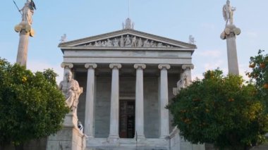 Atina Akademisi 'nde mermer sütunlar, Apollo ve Athena heykelleri ve Yunanistan' ın Atina kentinde mandalina ağaçları bulunan Yunan bayrağı. Popüler dönüm noktası ve seyahat yeri.