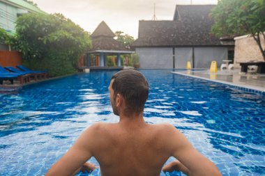 Tayland 'ın Phi Phi adasındaki berrak mavi sularda tropikal tatil köylerinde dinlenen erkek turist. Lüks seyahat ve turizm. Erkek yolcuların havuz başında eğlendikleri arka manzara. Huzur