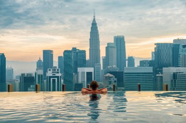 Erkek turist güneş doğarken sonsuz çatı üstü yüzme havuzunda dinleniyor, Kuala Lumpur, Malezya. Erkek gezgin şehir manzarasının keyfini çıkarıyor. Asya şehrinin finans ve iş merkezi modern.