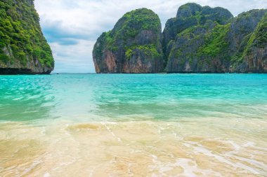 Maya Körfezi tropik kumlu plajı. Phi Phi adalarında turkuaz su okyanusu var. Krabi, Tayland 'da kimse yok. Boş kumsal, parlak mavi gökyüzünün altında yükselen yeşil uçurumlarla çevrili. Seyahat ve turizm