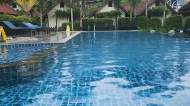 Berrak mavi sularla çevrili tropik tatil köyü yüzme havuzu, yemyeşil yeşillikler, palmiye ağaçları, güneş pansiyonları ve ahşap bungalovlar, Phi Phi Adası, Tayland. Lüks seyahat ve turizm.