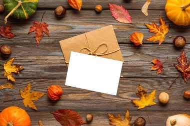 Kabaklardan yapılmış çerçevede boş tebrik kartı ve zarf, kurumuş yapraklar, çiçekler, fındıklar, ahşap arka planda kestaneler. Sonbahar ve Şükran Günü kompozisyonu. Düz yatıyordu. Model yap. Üst görünüm