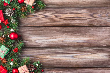 Köknar ağacı dalları, hediye kutuları, kırmızı süslemeler ve ahşap masa üzerinde çam kozalakları olan bir Noel arkaplanı. Düz yatıyordu. Mutlu yıllar ve kış tatilleri planı. Kopyalama alanı olan üst görünüm.