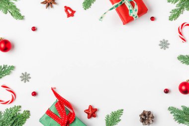 Noel çerçevesi köknar dalları, hediye kutuları, kırmızı süslemeler, beyaz arka planda şeker ve çam kozalaklarından yapılmış. Düz yatıyordu. Mutlu yıllar ve kış tatilleri. Üst görünüm.