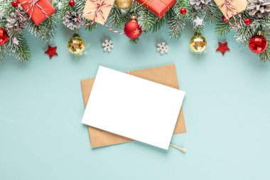 Noel tebrik kartı ve içinde karlı köknar ağacı dalları, hediye kutuları, süslemeler ve pastel mavi arka planda çam kozalakları olan bir zarf. Düz yatıyordu. Model yap. Mutlu yıllar ve kış tatilleri daveti