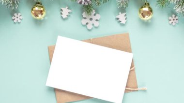 Noel tebrik kartı ve içinde karlı köknar ağacı dalları, şenlikli süslemeler ve pastel mavi arka planda çam kozalakları olan bir zarf. Düz yatıyordu. Model yap. Mutlu yıllar ve kış tatili davetiyeleri. Üst