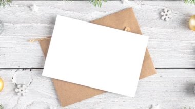 Karlı köknar dallarından yapılmış çerçevede Noel tebrik kartı ve zarf, altın madalyalar, beyaz ahşap arka planda çam kozalakları. Düz yatıyordu. Model yap. Mutlu yıllar ve kış tatilleri daveti