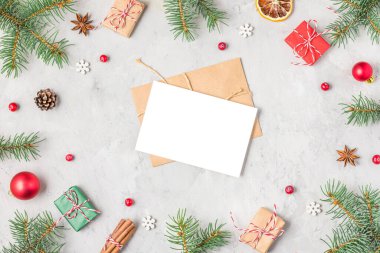 Köknar dalları, kırmızı süslemeler, hediye kutuları, gri beton arka planda Noel yemeği ve çam kozalaklarından oluşan çerçevedeki Noel tebrik kartı. Düz yatıyordu. Model yap. Mutlu yıllar davetiyesi. Üst görünüm.