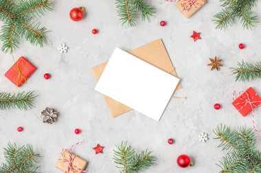 Köknar dalları, kırmızı süslemeler, hediye kutuları ve gri beton arka plandaki çam kozalaklarından oluşan çerçevedeki Noel tebrik kartı. Düz yatıyordu. Model yap. Mutlu yıllar davetiyesi. Üst görünüm.