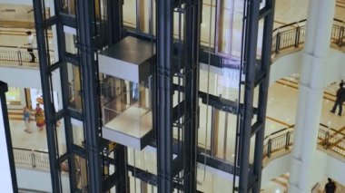 Kuala Lumpur, Malezya - 5 Haziran 2024: Petronas İkiz Kulelerindeki Suria KLCC alışveriş merkezi içi modern cam asansörle birden fazla kat ve balkonlarda insanların bulunduğu alışveriş merkezinin içine taşınıyor.