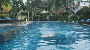 Tatil köyü havuzunda yüzen adam, çevresi tropik yemyeşil yeşilliklerle çevrili, Tayland 'ın Phi Phi adasındaki berrak mavi sularda ferahlatıcı bir şekilde yüzüyor ve dinleniyor. Lüks seyahat ve turizm.