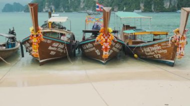 Krabi, Tayland - 1 Haziran 2024: Geleneksel uzun kuyruklu tekneler turkuaz su ve Phi Phi Don Adası, Krabi, Tayland 'daki yemyeşil kireçtaşı kayalıkları ile kıyıya demirli. Popüler turistik tatil
