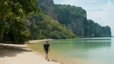 Tayland 'ın başkenti Krabi' de turkuaz su ve uçurumlarla Railay kumsalında yürüyen bir turist. Asya 'da popüler turistik tatil beldesinde erkek gezgin.